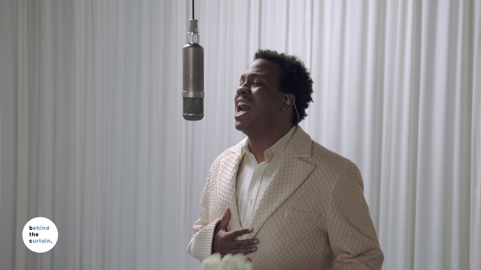Lee Lewis performing at a vintage microphone, surrounded by white curtains